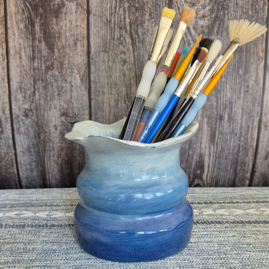 Blue ceramic holder with paintbrushes on a wooden surface