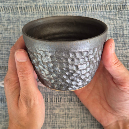 Hand holding a textured ceramic cup against a woven fabric background