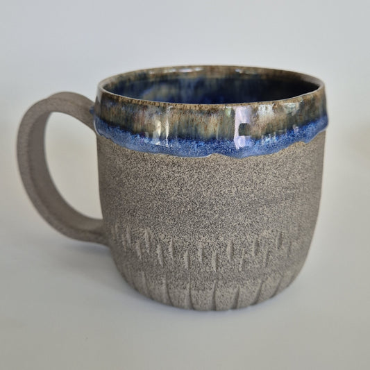 Ceramic mug with textured surface and blue interior on a light gray background