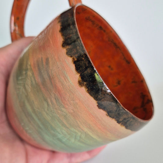 Hand holding a ceramic mug with a unique design on a plain background