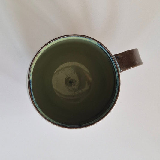 Inside of Anthracite brown stoneware mug with green flowy glaze. On a plain background