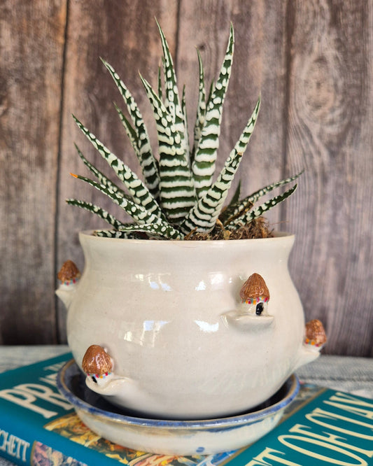 Decorative pot with a plant on a book titled 'Feet of Clay' against a wooden background