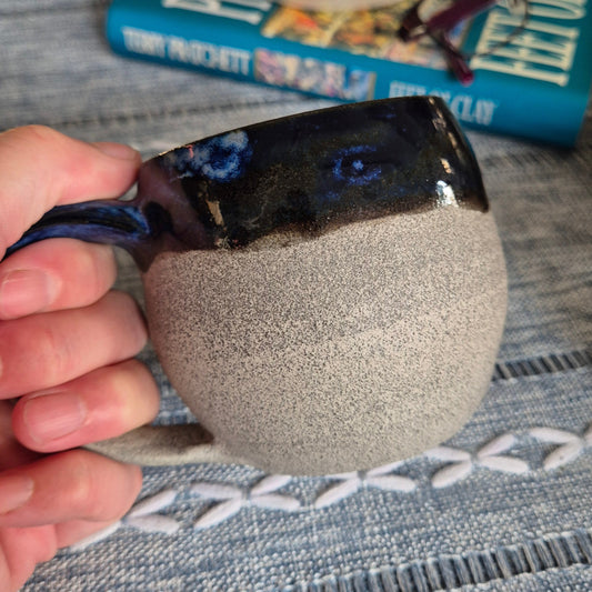 Person holding a textured gray mug with a blurred background