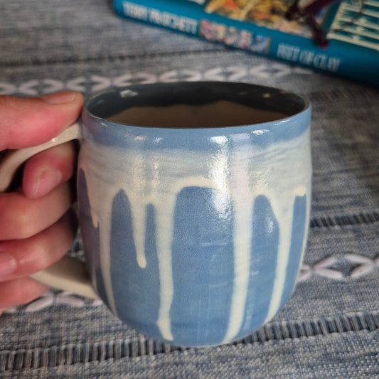 Hand holding a blue and white ceramic mug with a blurred background