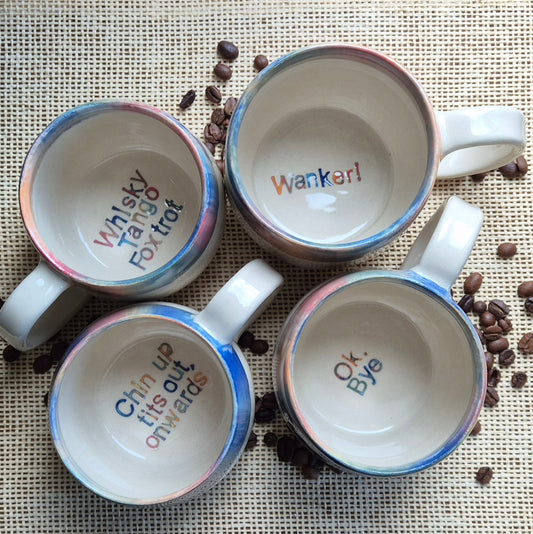 Four mugs with humorous text on a surface with coffee beans