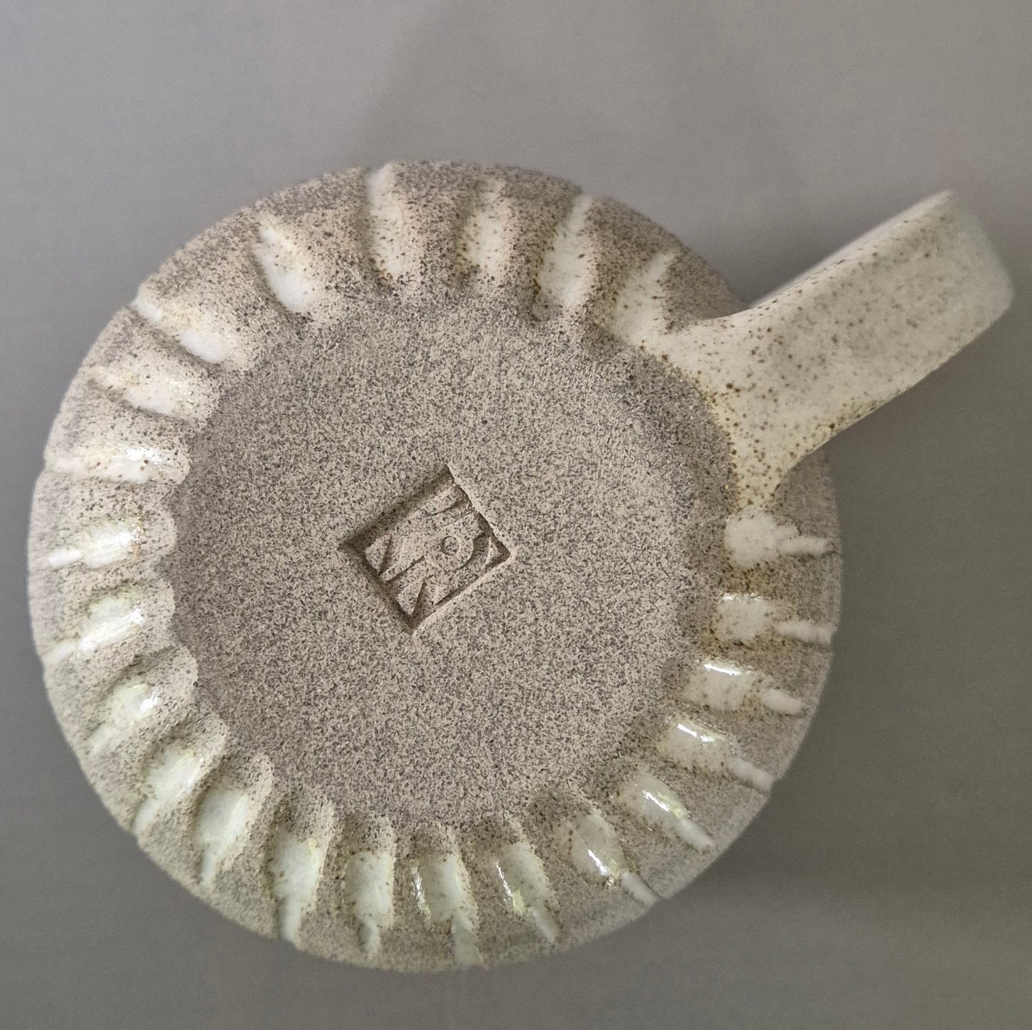 Base of a ceramic mug with textured design and handle on a gray background