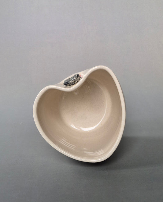 Photo showing the top of a small white heart-shaped stoneware pot On a grey background.