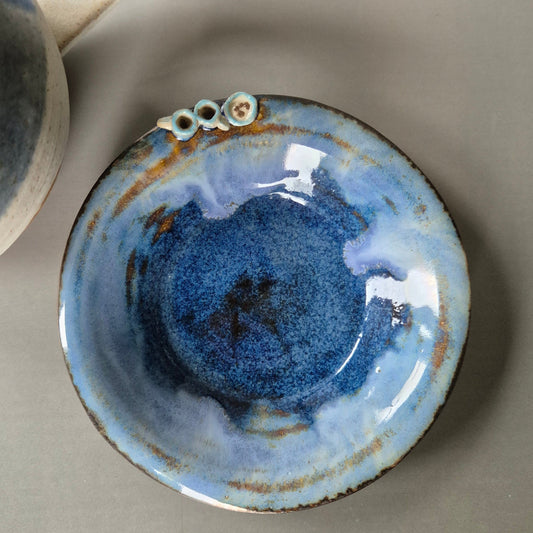 Handmade stoneware trinket dish with tiny tea cups and cookies, shown beside a mug on a neutral background.
