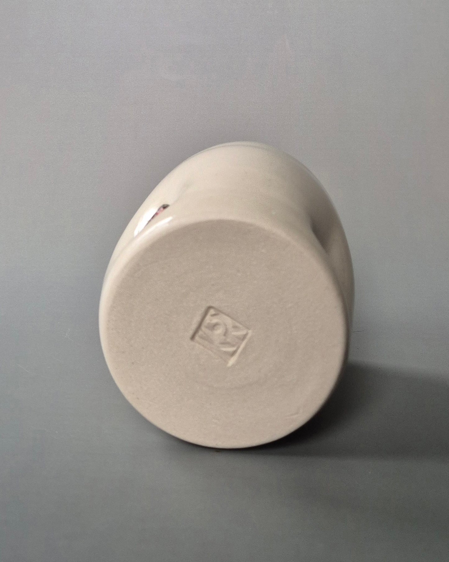 Base of a small white stoneware pot displaying the makers mark, on a grey background