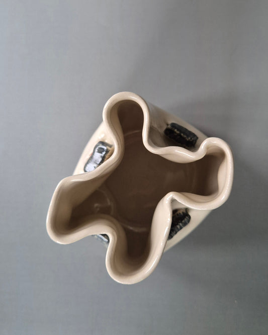 Top view of a small white stoneware pot folded to embrace 4 tiny cottages. On a grey background