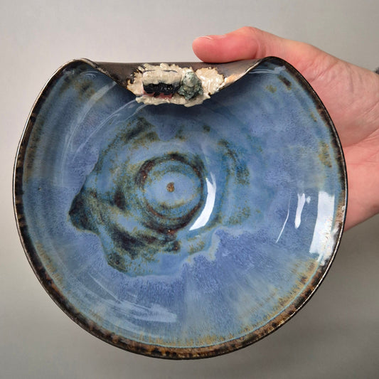 Hand holding a blue ceramic bowl with a textured surface on a gray background