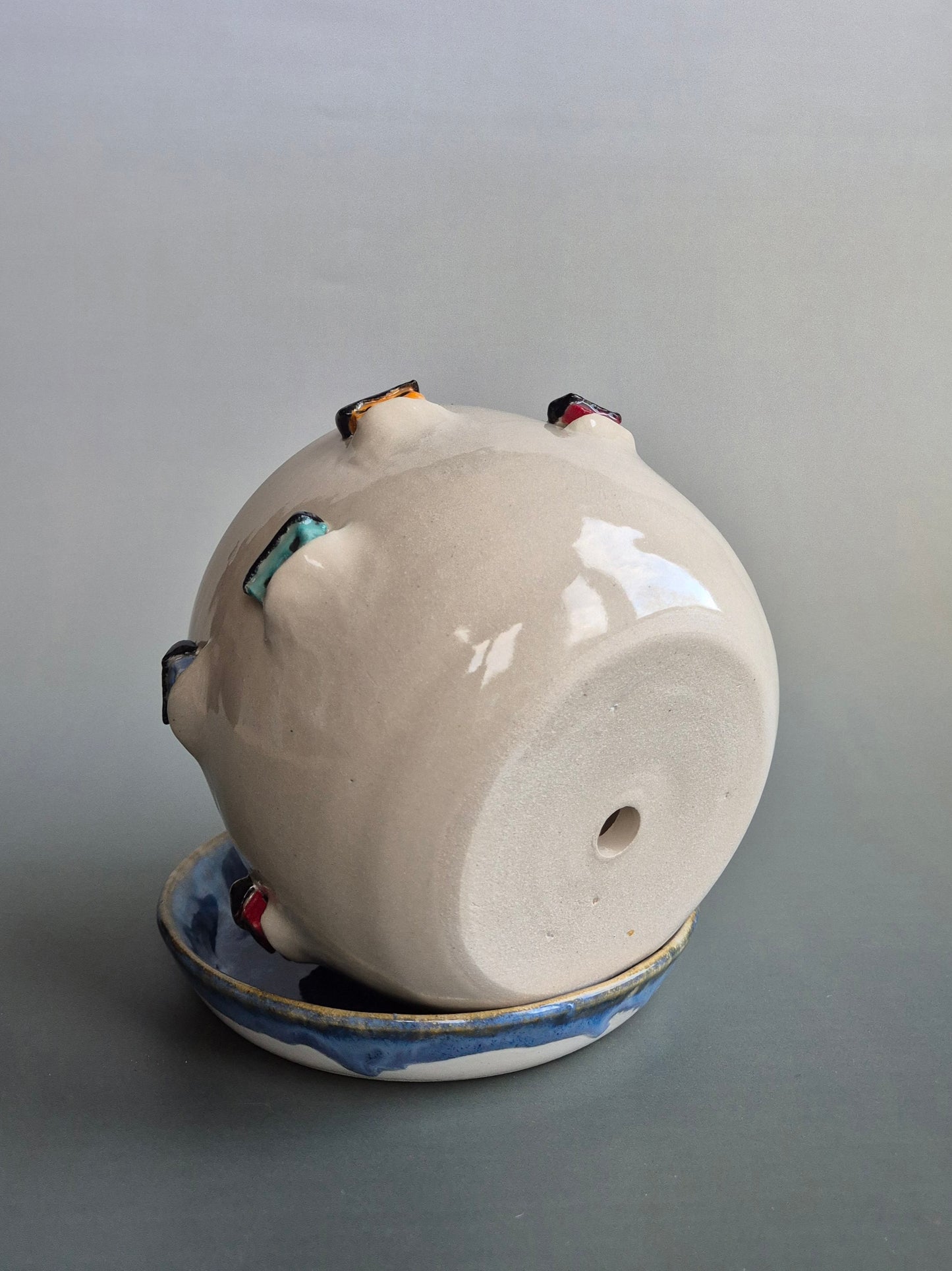 Base of a ceramic planter decorated with colourful tiny houses to show the drainage hole. On a blue saucer with a plain background