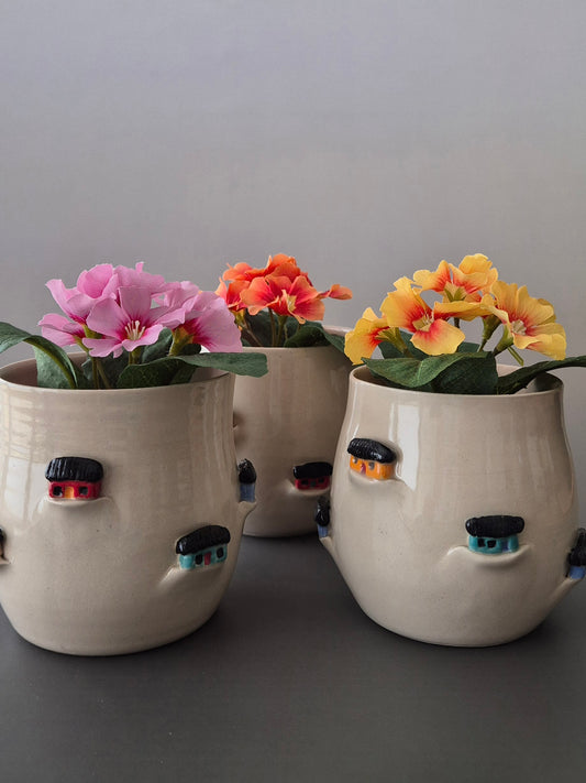 Three ceramic house planters with flowers on a gray background