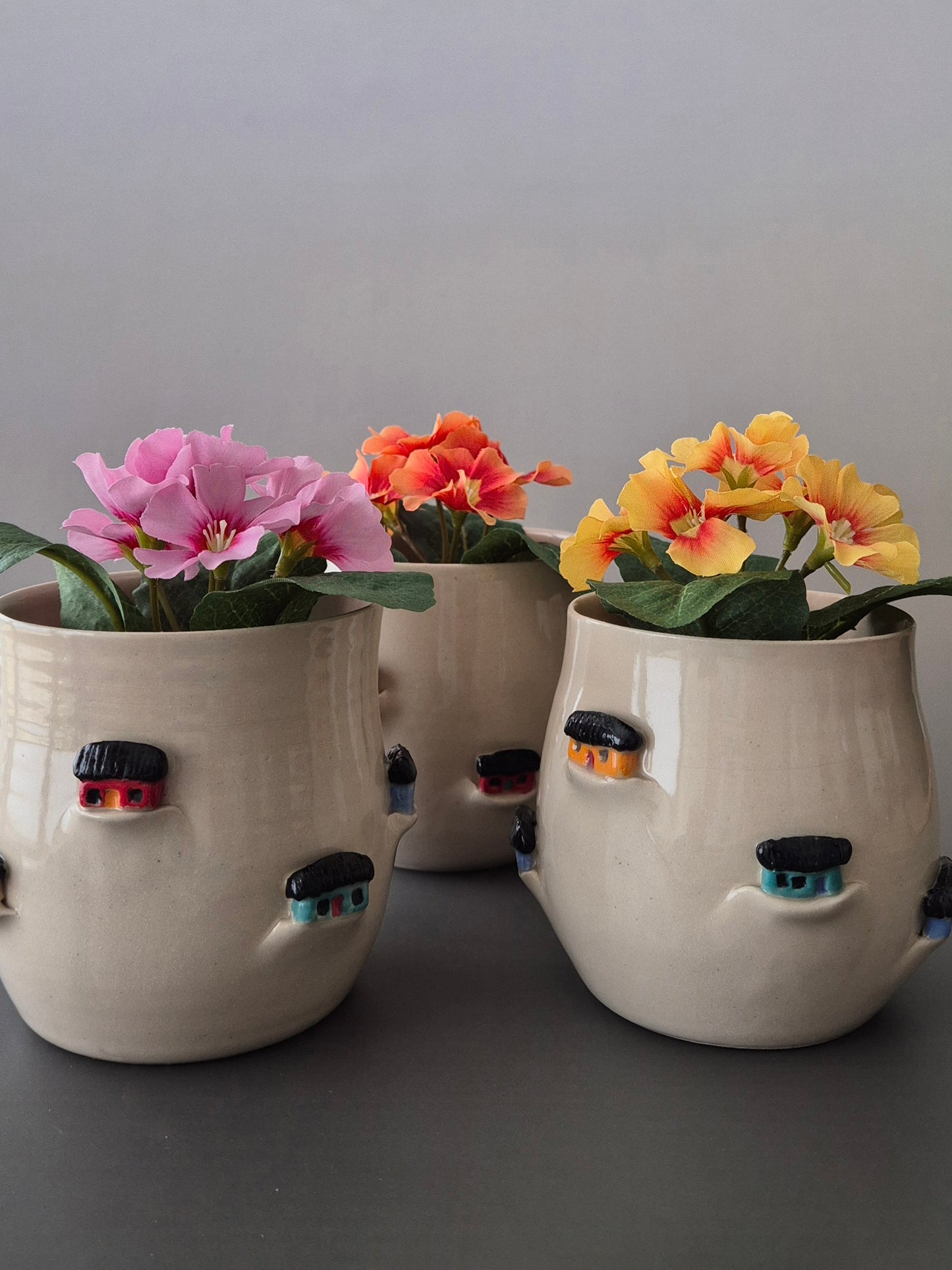 Three ceramic planters with flowers on a gray background