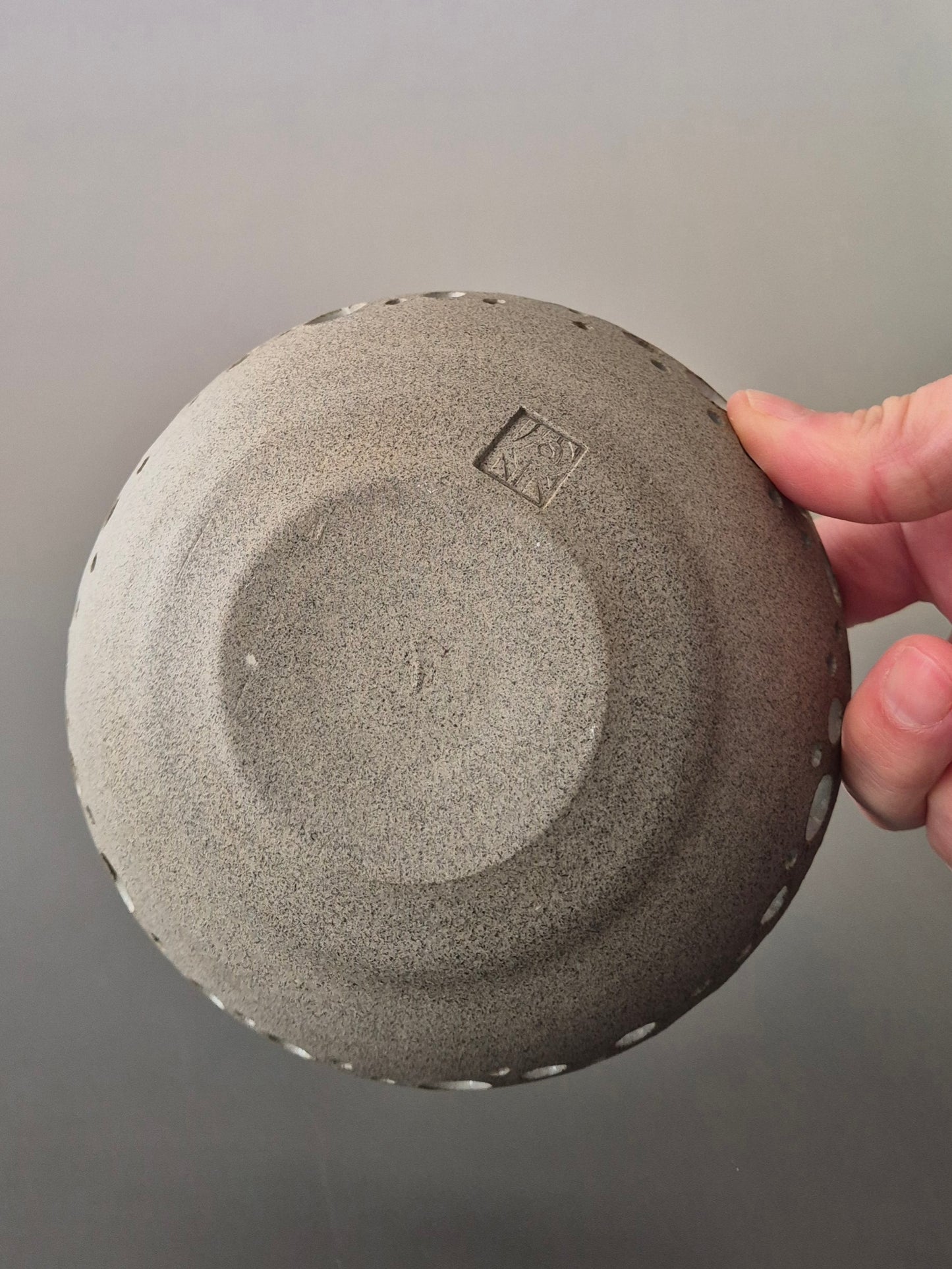 Person holding a textured gray dish to show the base against a neutral background