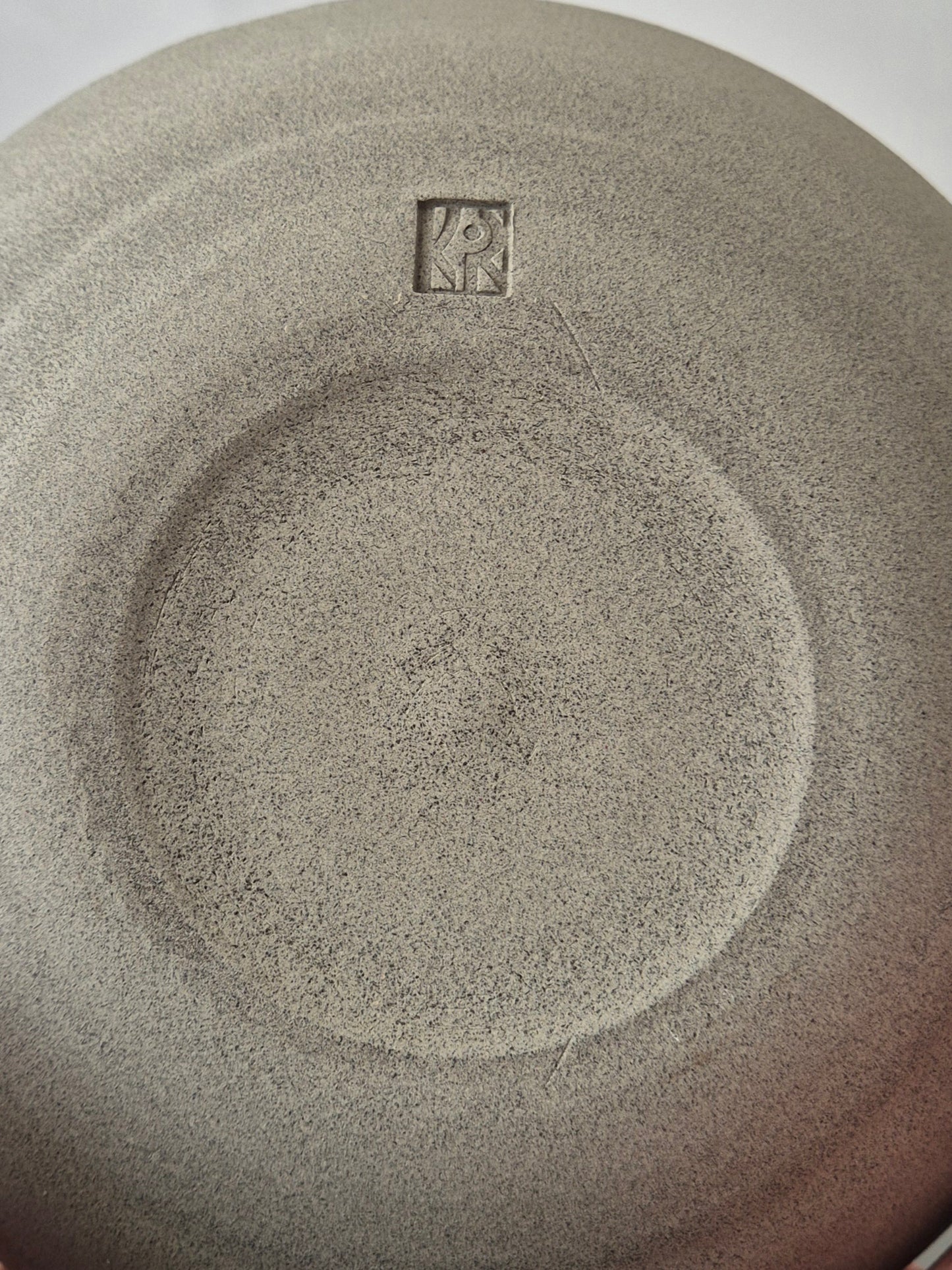 Close-up of the base of a textured ceramic bowl with the potters makers mark in the center.