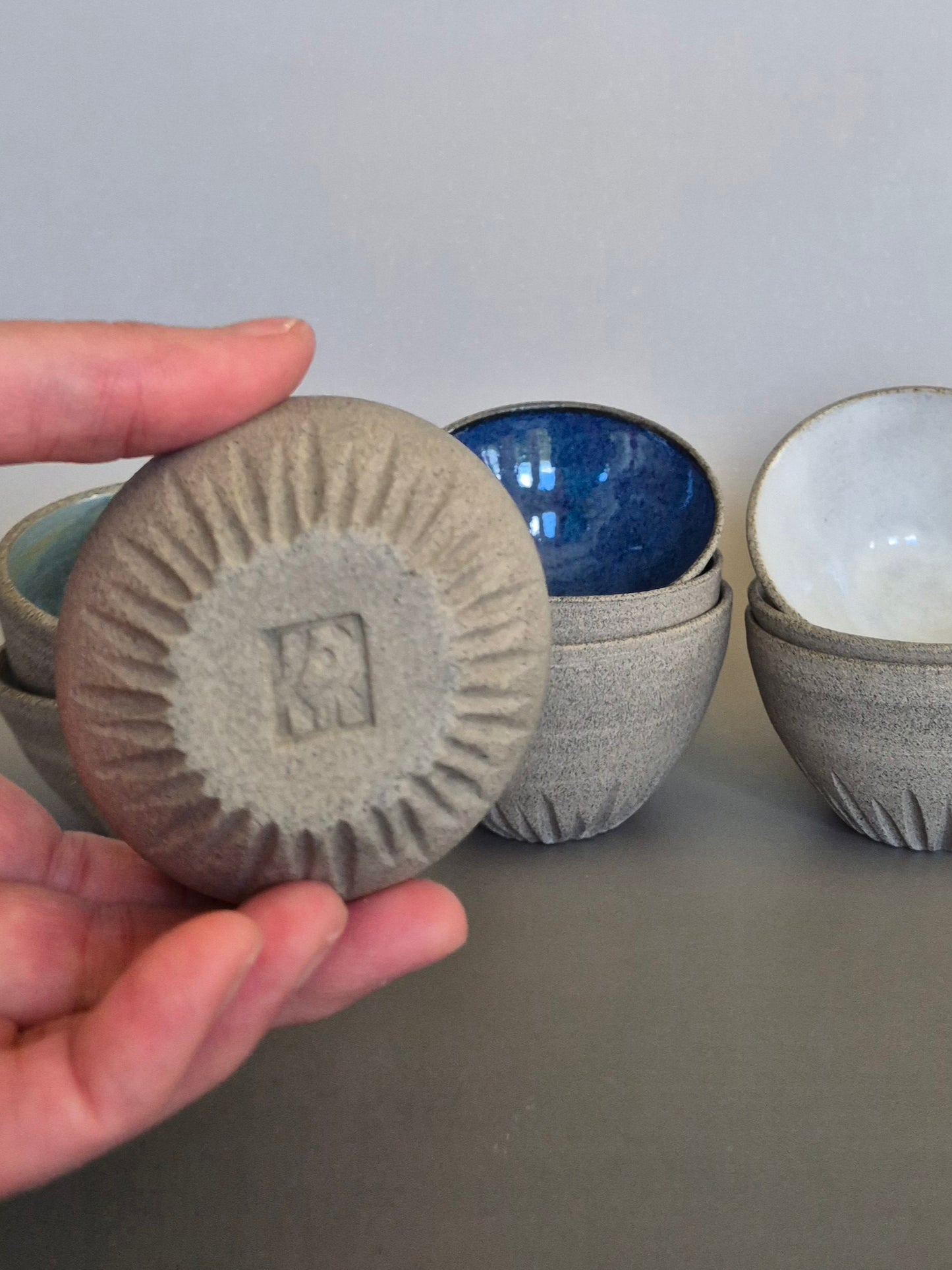 Hand holding a textured ceramic bowl to show the base over stacked ceramic bowls on a neutral background