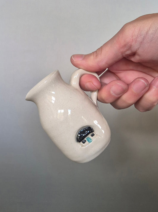 Hand holding a small white ceramic pitcher with a gray background