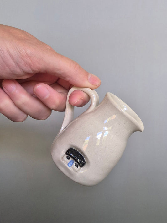 Hand holding a small ceramic pitcher with a plain background