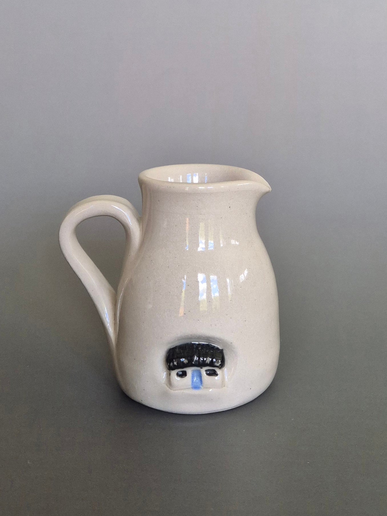 White ceramic pitcher with a house design on a gray background