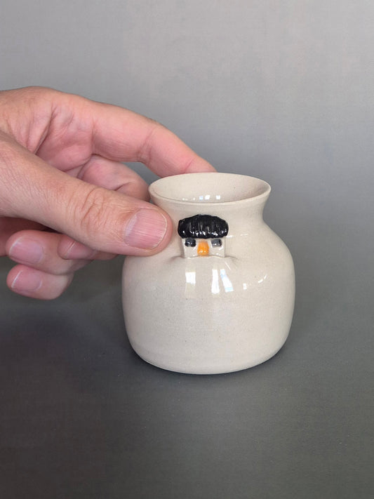 A hand holding a small white ceramic bottle or bud vase. On a plain background