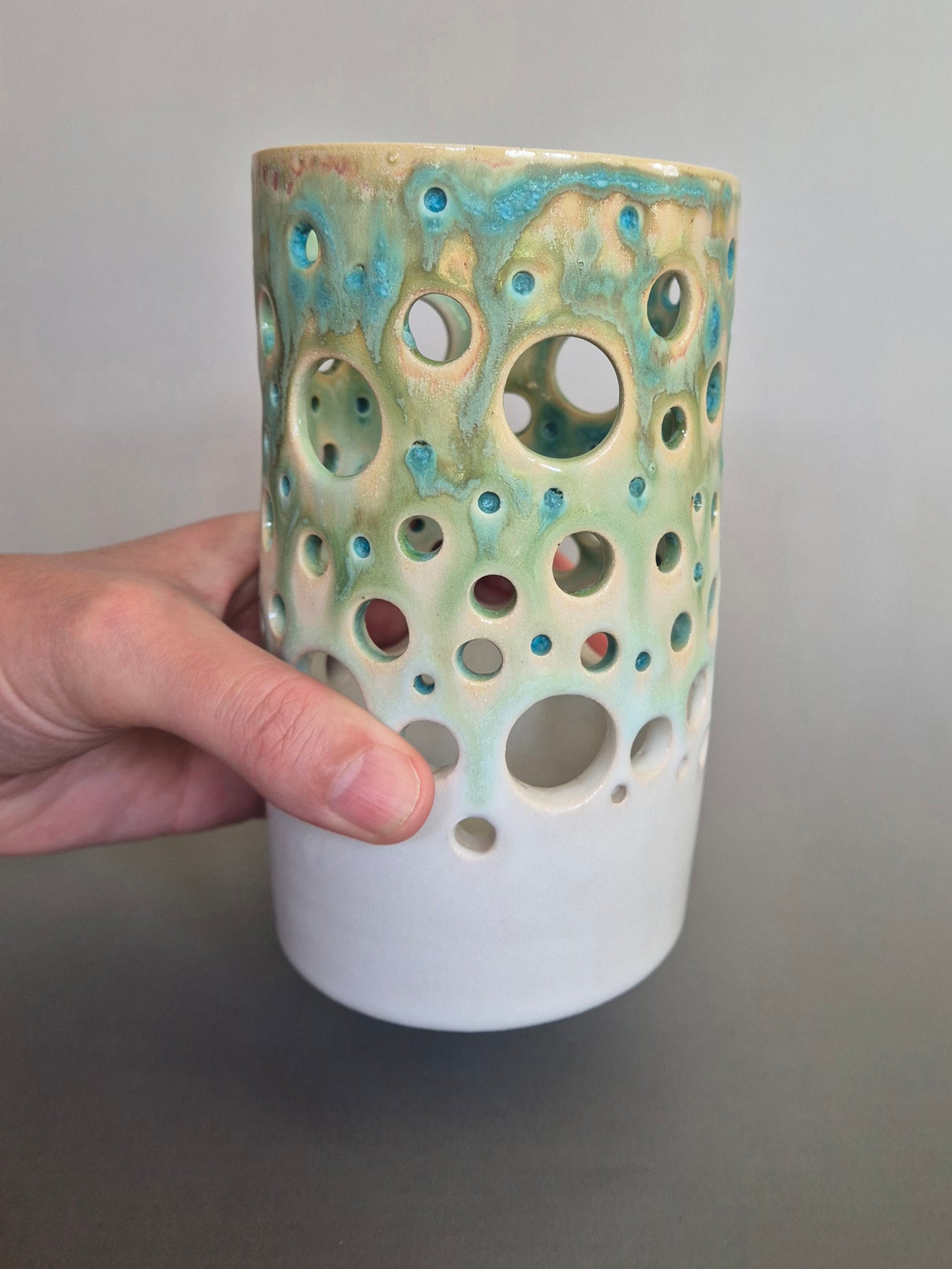 Ceramic vase with textured surface held by a hand against a neutral background