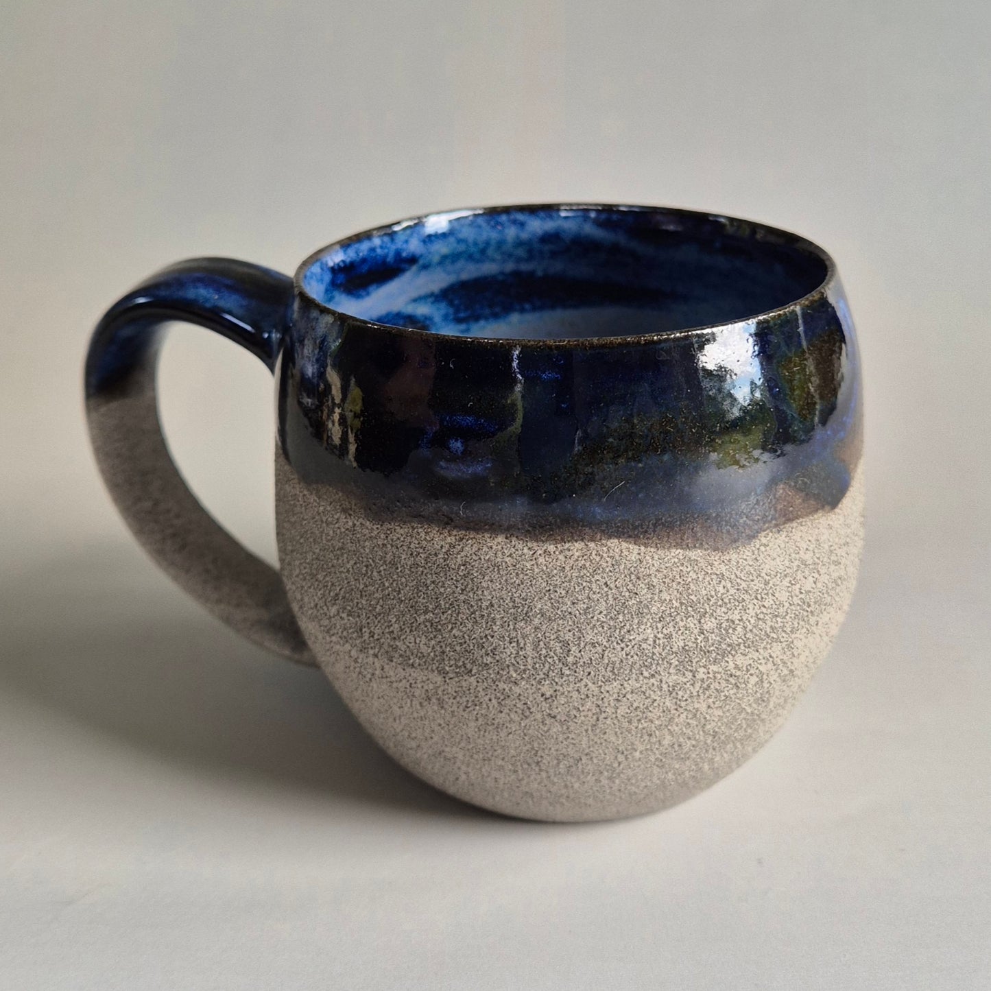 Ceramic mug with blue interior and textured beige exterior on a light gray background