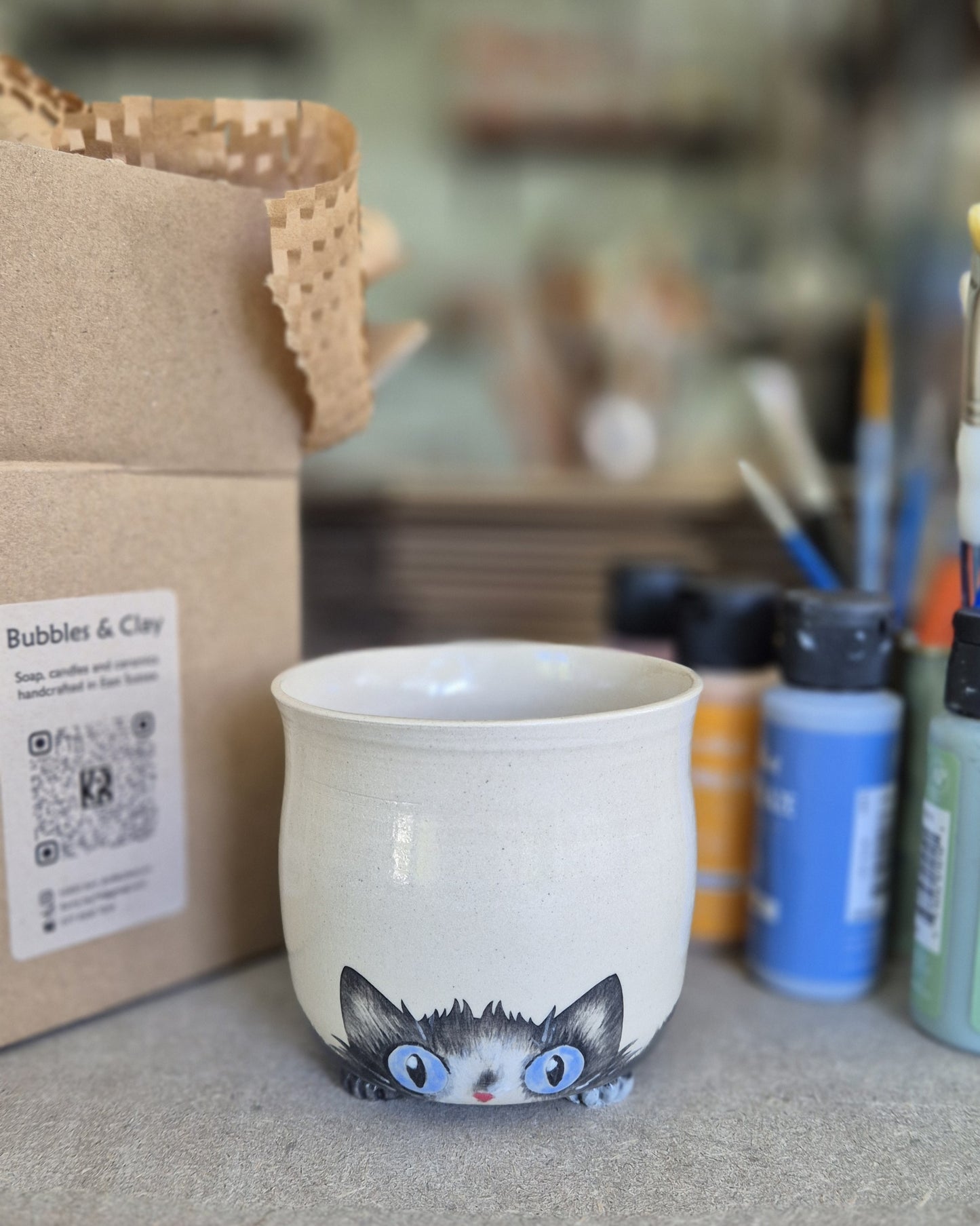 Ceramic mug with a cat design on a surface with art supplies in the background