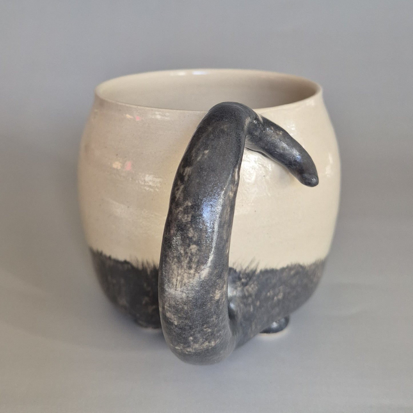 Ceramic cat mug with a black tail handle on a gray background