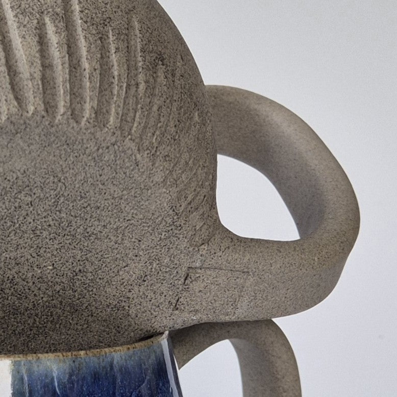 Close-up of a textured ceramic mug and handle on a light gray background