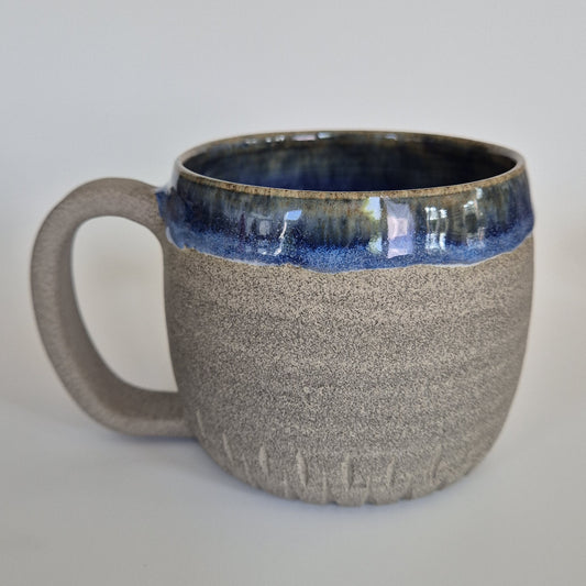 Ceramic mug with blue interior and textured exterior on a light gray background