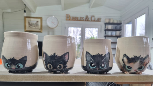 A row of 4 hand-painted pottery cat mugs in the Bubbles & Clay studio