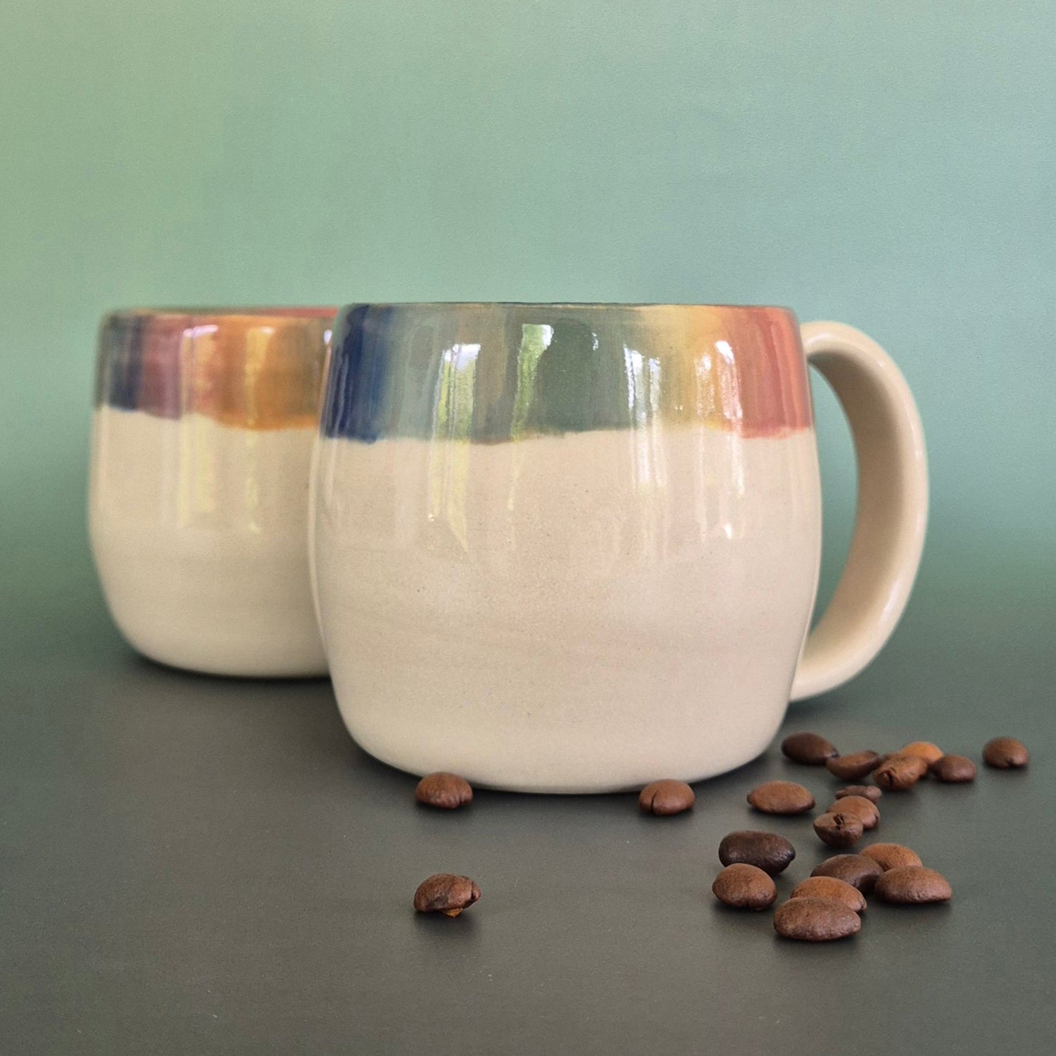 A pair of colourful mugs with a green background and coffee beans