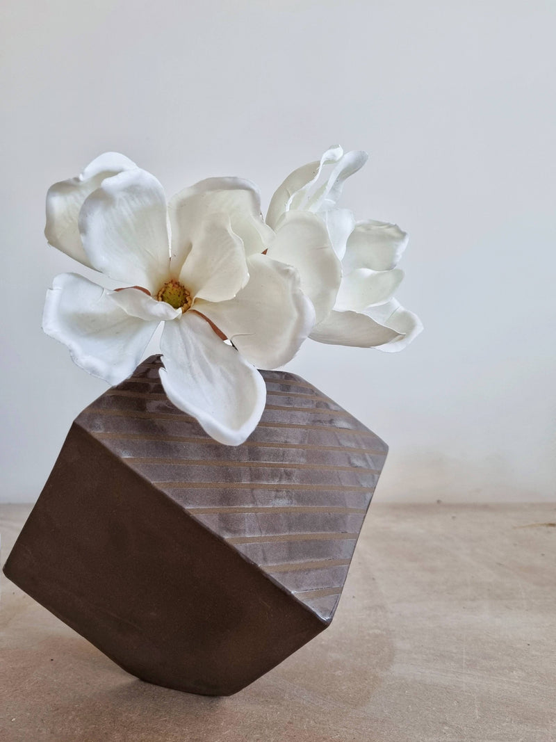 Square brown ceramic vase with a white flower on a light wooden surface