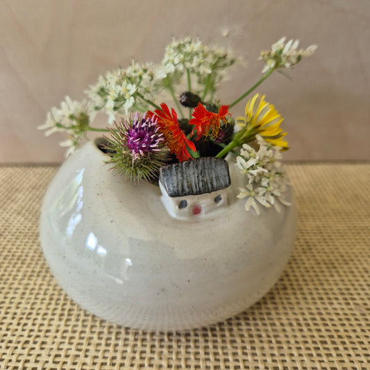 Small tiny house bud vase with wildflowers. on a patterned beige table-cloth