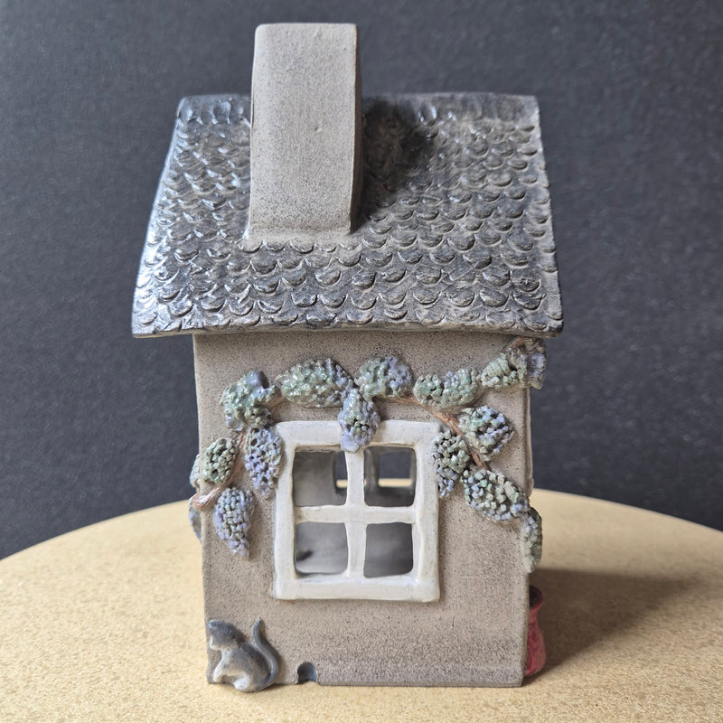A small decorative house with textured walls and windows on a dark surface.