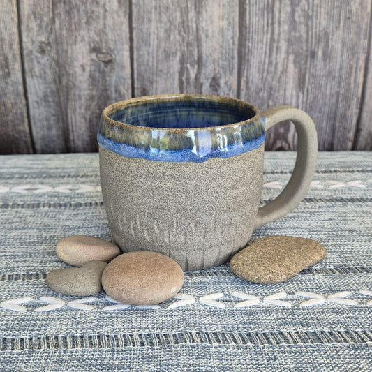 Ceramic mug with blue interior on a textured surface with stones