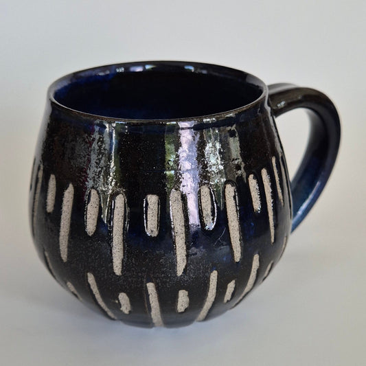 Black ceramic mug with carved abstract patterns on a light gray background