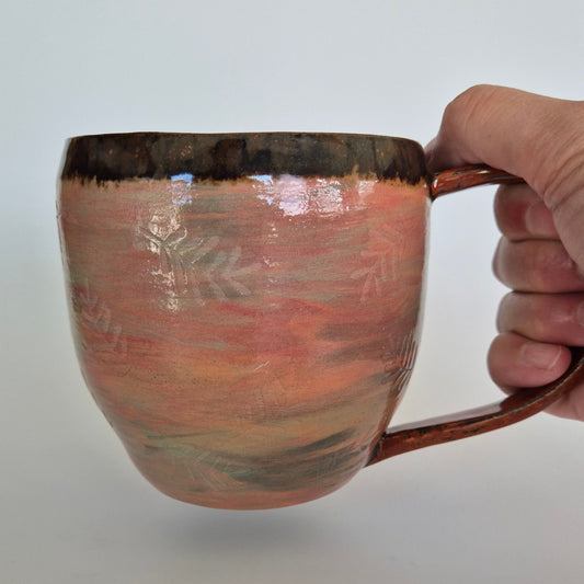 Hand holding a ceramic mug with a handle against a plain background