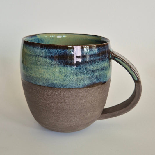 Anthracite brown stoneware mug with green flowy glaze. On a plain background