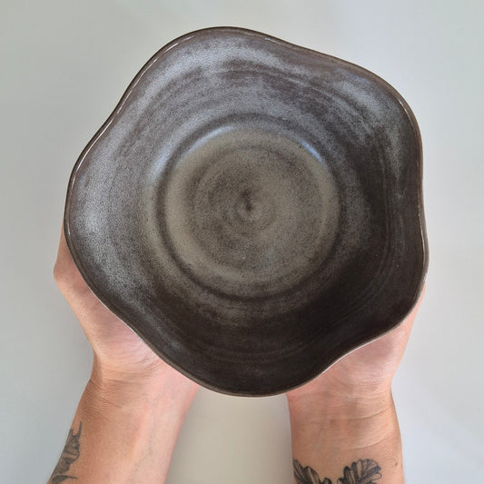 Person holding a brown ceramic bowl with tattooed arms on a light background
