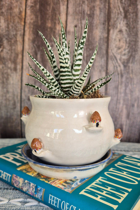 Decorative pot with a plant on a book titled 'Feet of Clay' against a wooden background