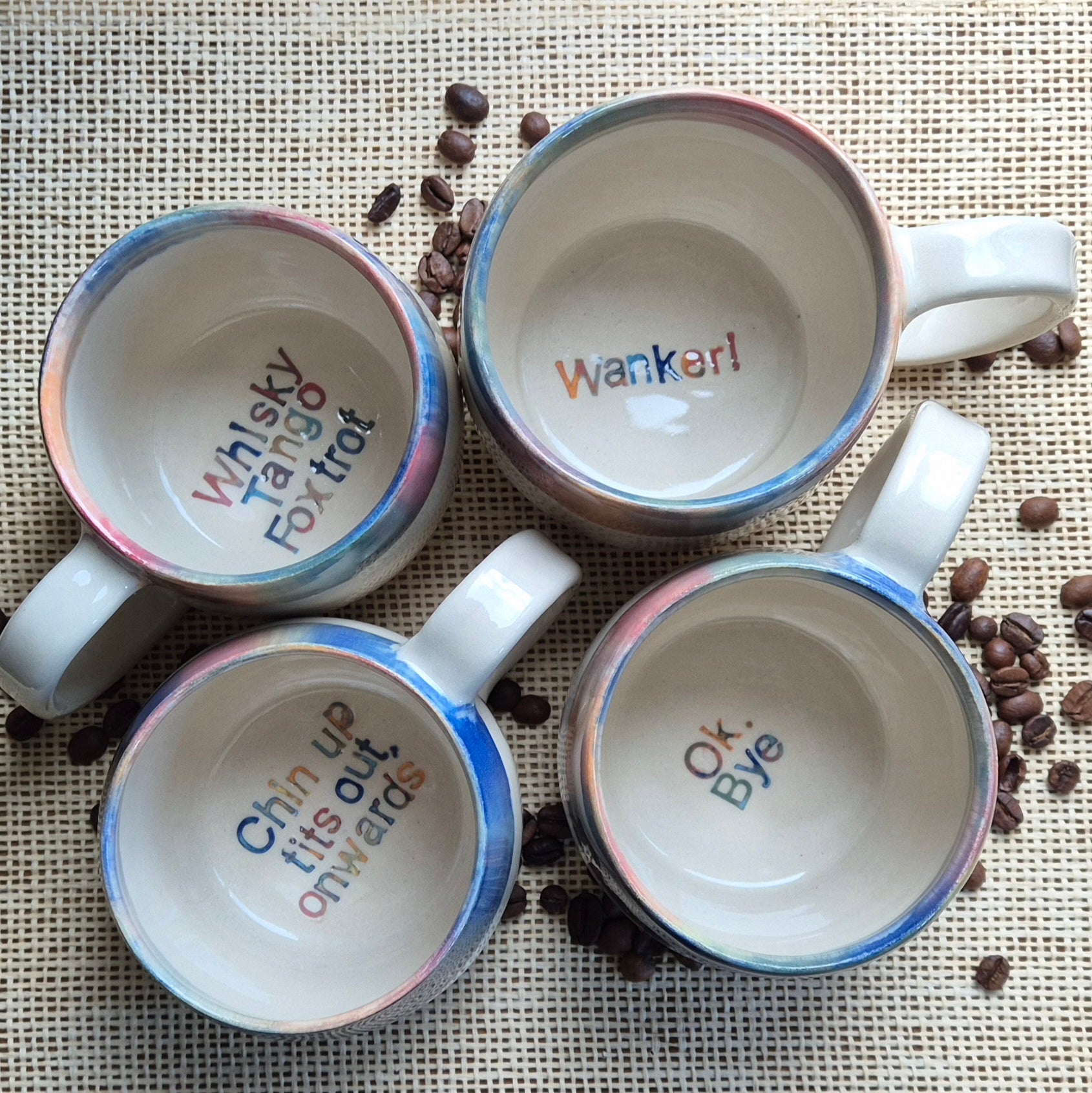 Four mugs with humorous text on a surface with coffee beans