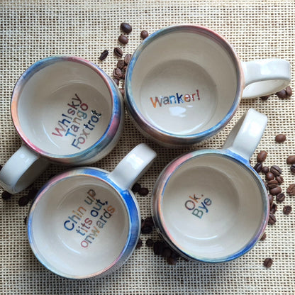 Four mugs with humorous text on a surface with coffee beans