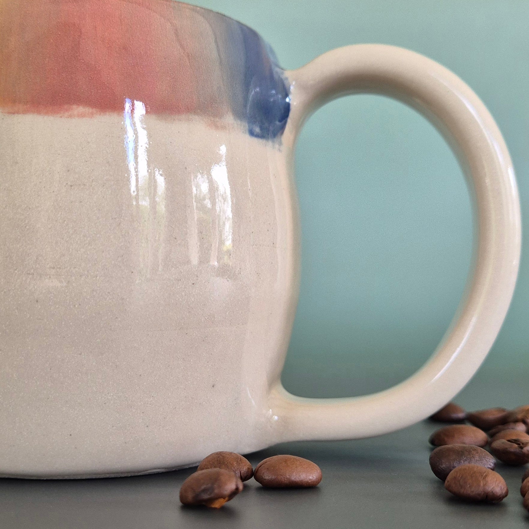 White ceramic mug with a handle on a gray surface with coffee beans