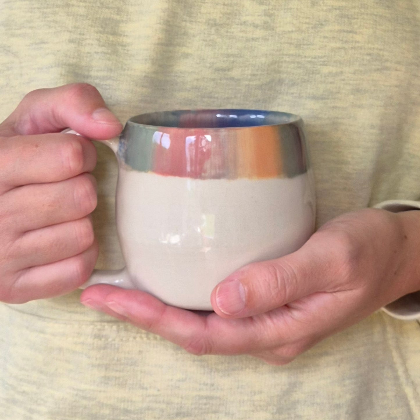 Person holding a ceramic mug with a gradient color design on a textured fabric background