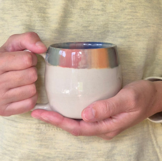 Person holding a ceramic mug with a gradient color design on a textured fabric background