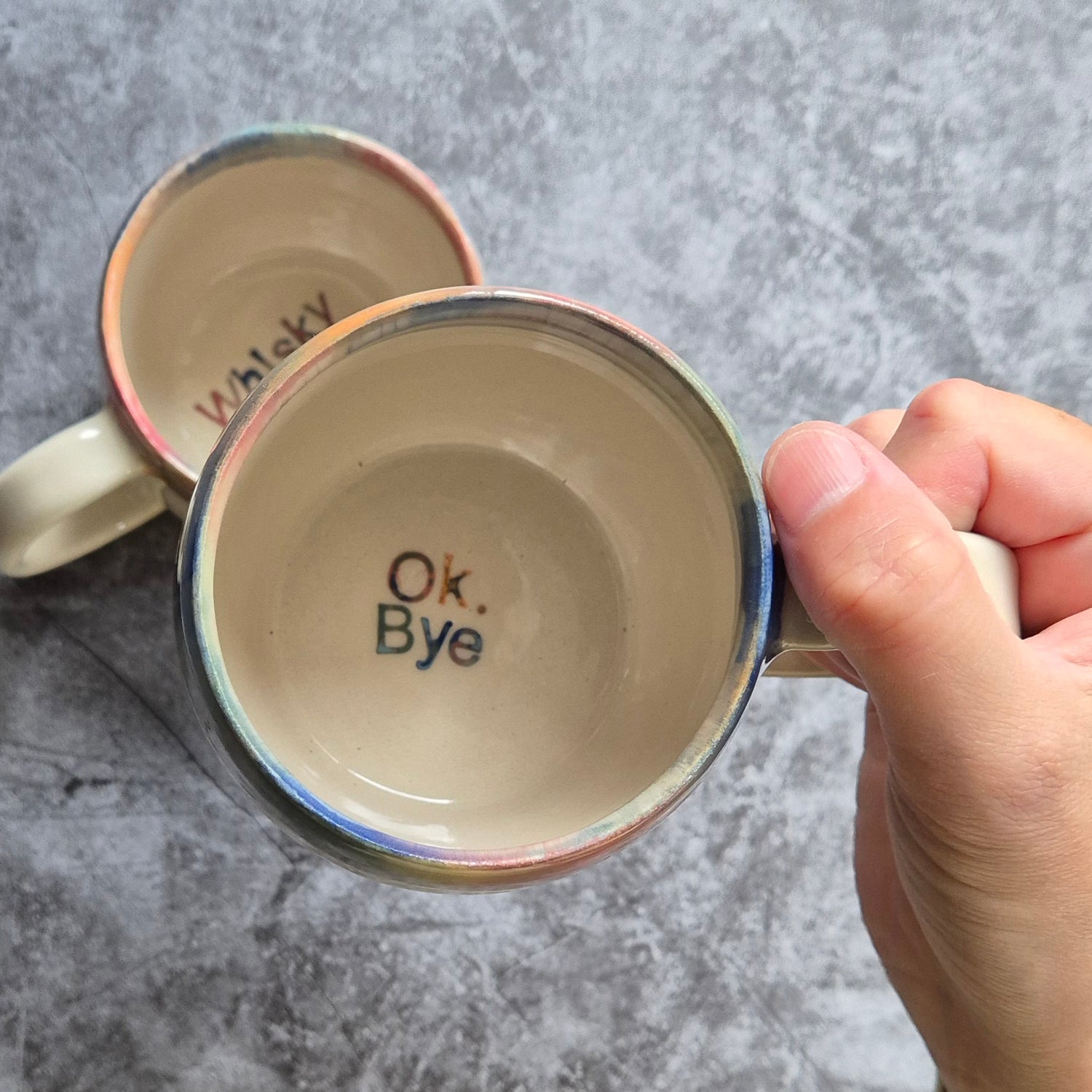 Mug with 'Ok, Bye' text held by a hand on a gray background