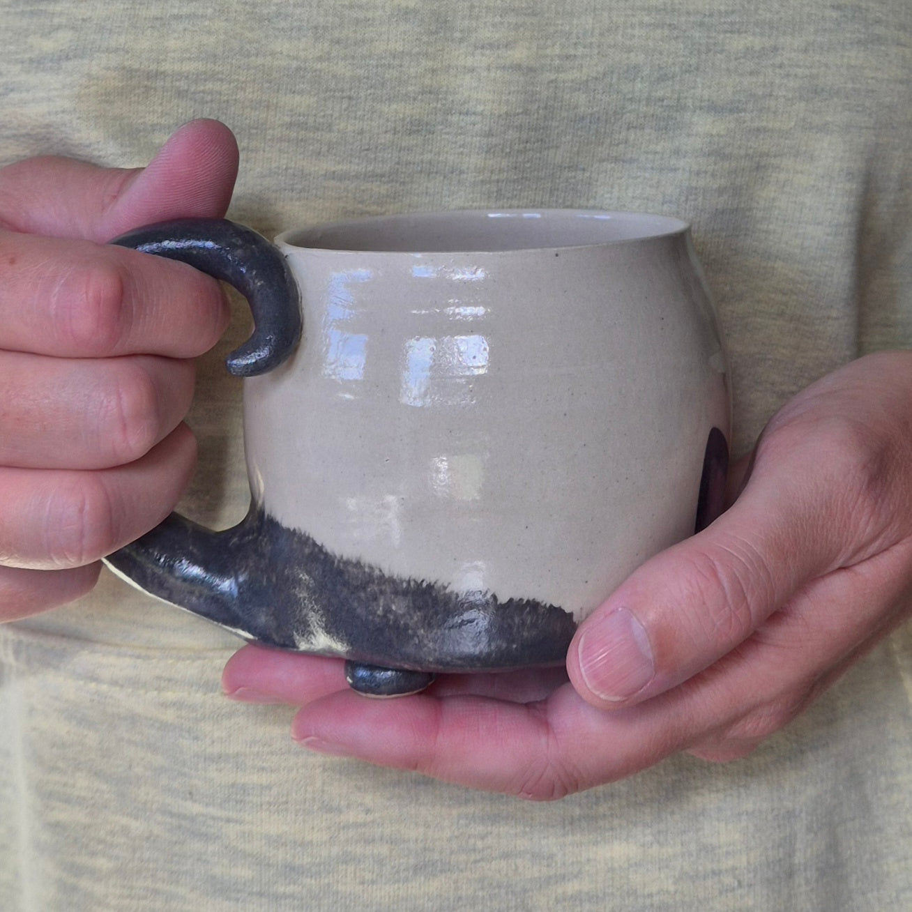 Person holding a ceramic mug with black tail handle against a neutral background