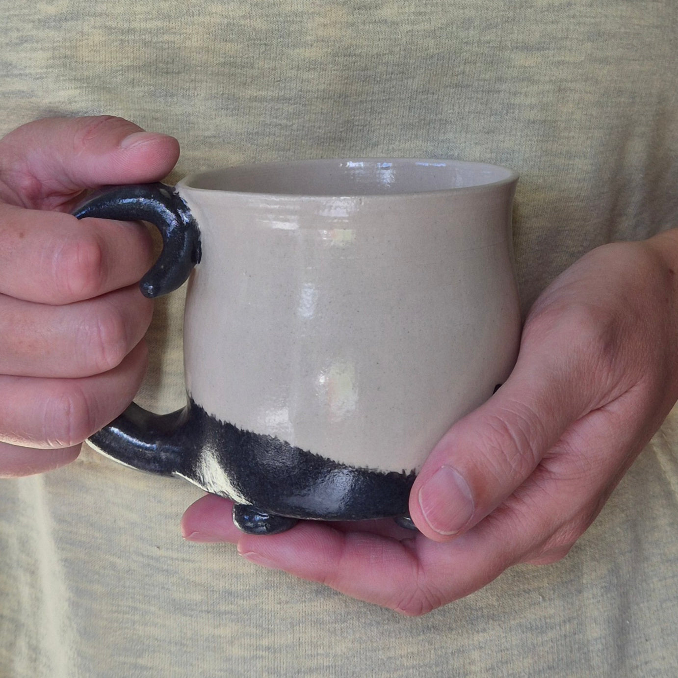 Person holding a ceramic cat mug with a black tail on a neutral background